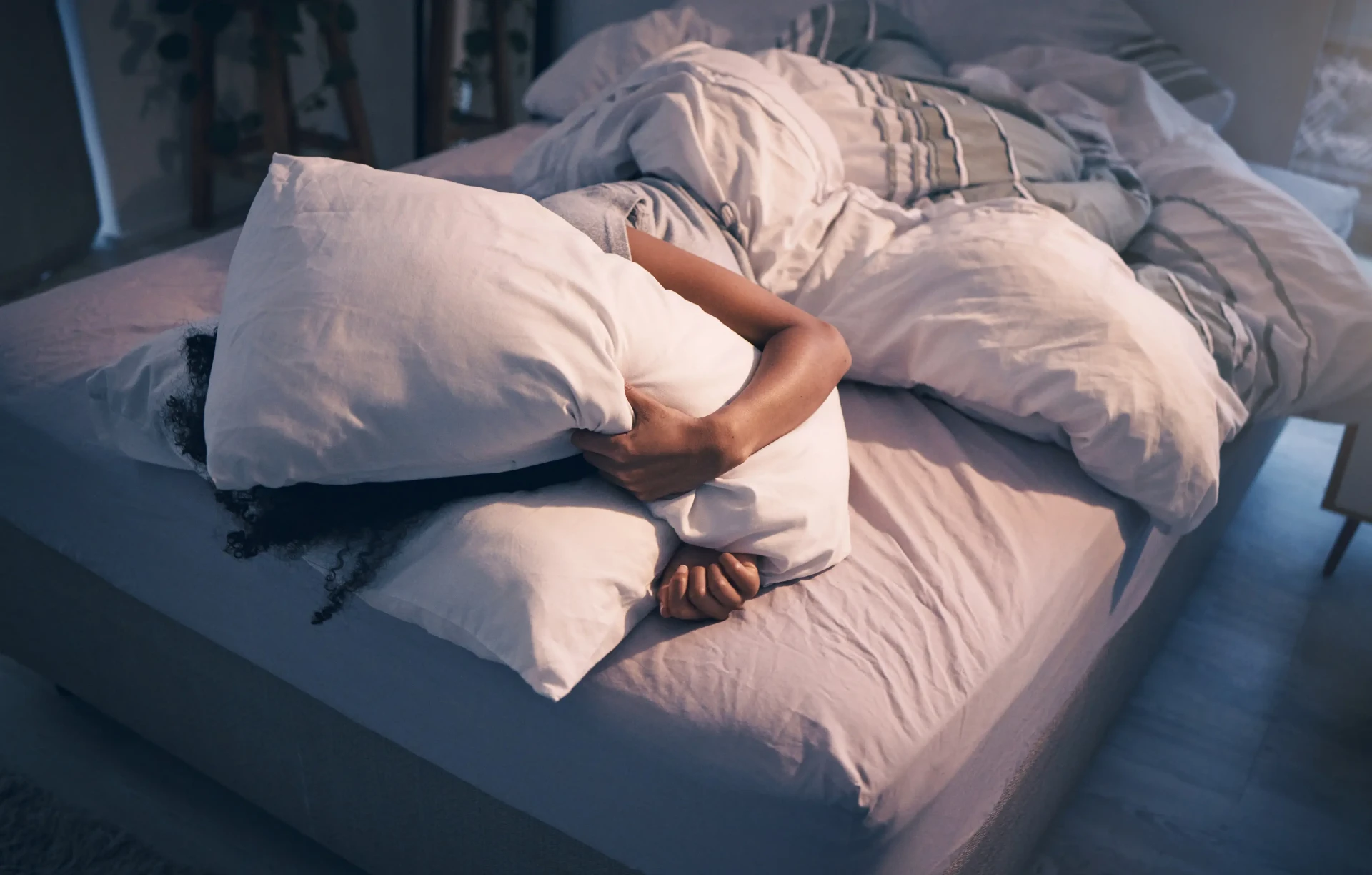 Person lying in bed at night holding a pillow over their face